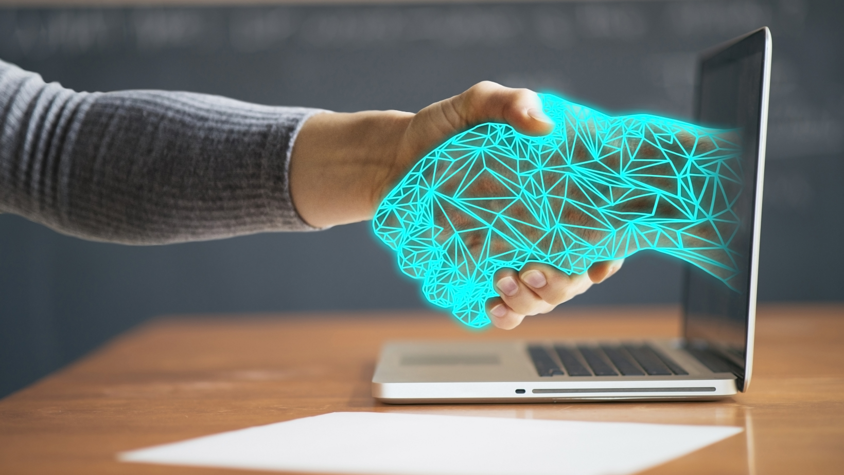 person shaking hand with digital AI robot hand reaching through laptop screen