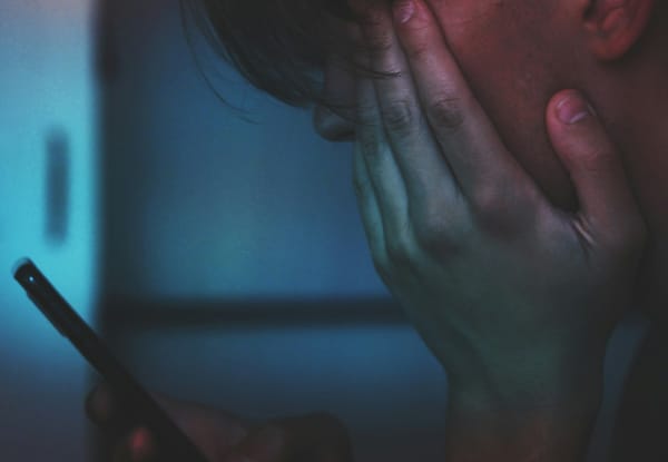 Young man sitting staring out his smartphone looking stressed and tired. 